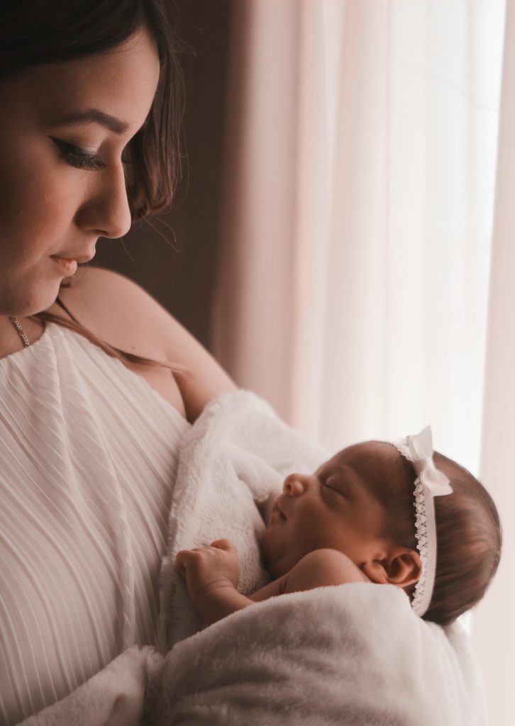 zipwp-image-3398675 Tender moment of a mother holding her newborn child by a window, capturing love and warmth.